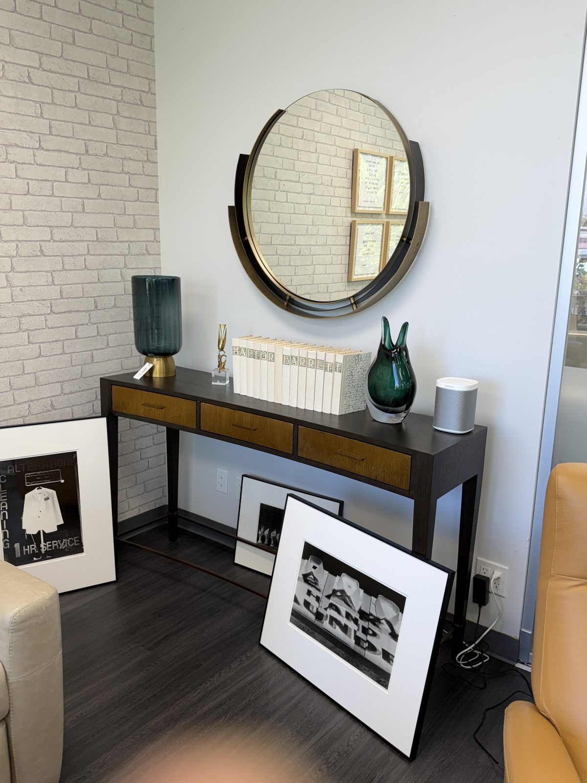 Console table styled with Haptor Barrett-branded books, a brushed brass and bronze round mirror, and decorative glass — inside the Haptor Barrett showroom