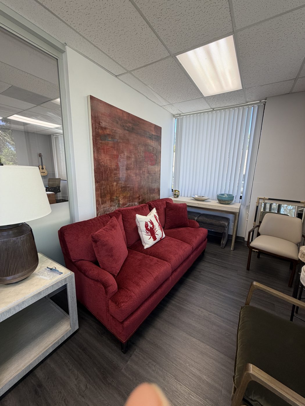 Crimson red velvet sofa with a lobster-print accent pillow, abstract painting, and warm wood tones in the Haptor Barrett showroom